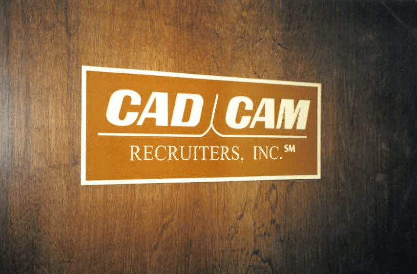 Sign for CAD/CAM Recruiters, Inc. displayed on a wooden background, indicating a recruitment agency specializing in CAD/CAM fields.