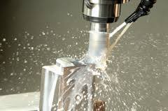 A high-speed CNC milling machine cutting into an aluminum workpiece, with coolant spray and metal shavings being ejected.